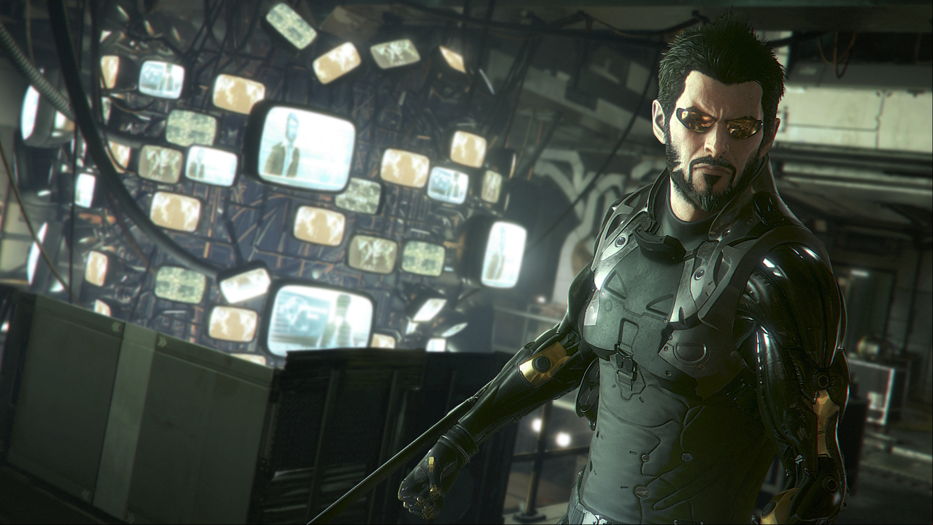 Adam Jensen scowls as he stands in front of a complex display of old CRT monitors wired to the ceiling, displaying his arm-mounted blades. 