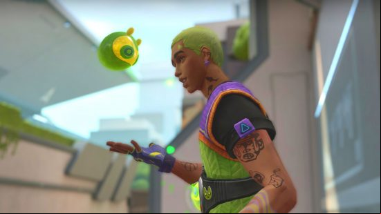 A Latino man with bright neon green hair wearing a neon green and purple tactical vest holds out his hand as a small green slime with a yellow superhero-style mask looks down at him