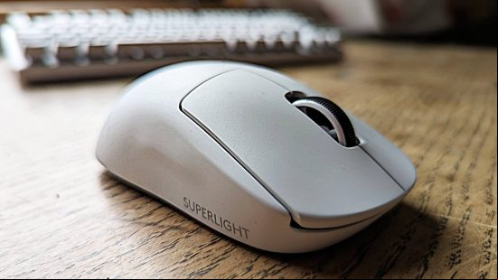 Logitech G Pro X Superlight 2 gaming mouse review: a white Logitech mouse sits on a wooden surface with a blurred keyboard in the background.