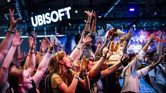 A crowd of people cheers and raise their hands with a huge Ubisoft logo in the background