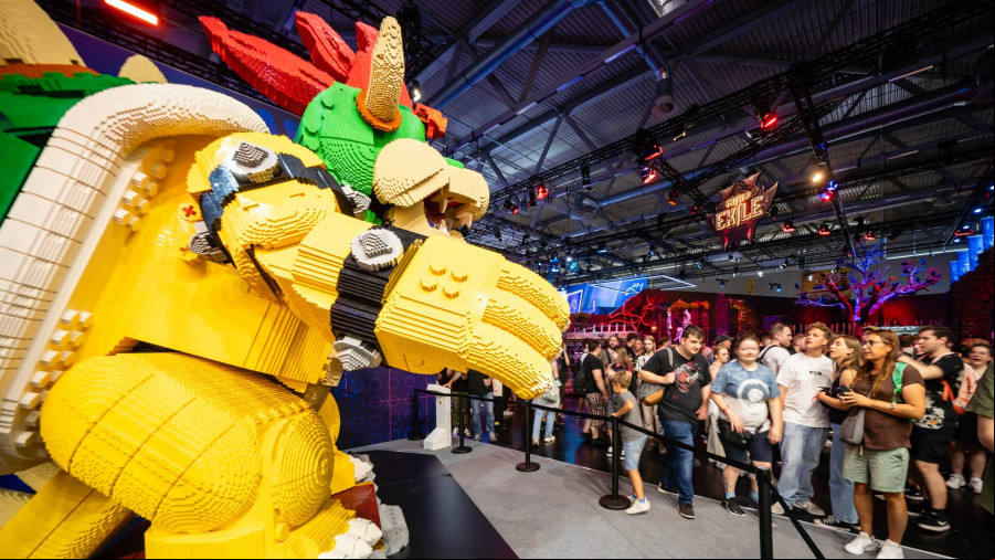 A huge LEGO figure of Super Mario villain Bowser stands behind a cord as a group of people look at it
